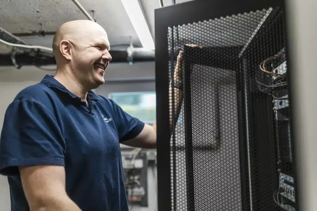Mann steht in Serverraum und lächelt, während er eine Tür hält